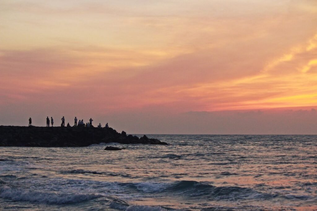 pexels photo 10575835 10575835 Captivating sunset at Kanyakumari, TN, India, with silhouettes of people on the rocky shore.