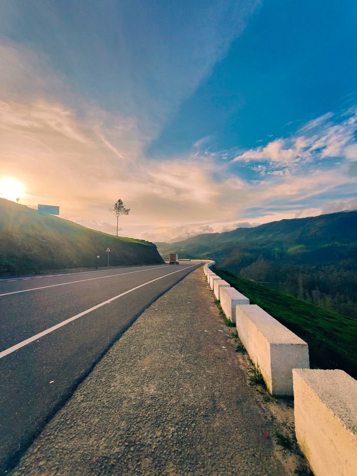 Serene road in Munnar, India with stunning sunset views over rolling hills and open countryside.