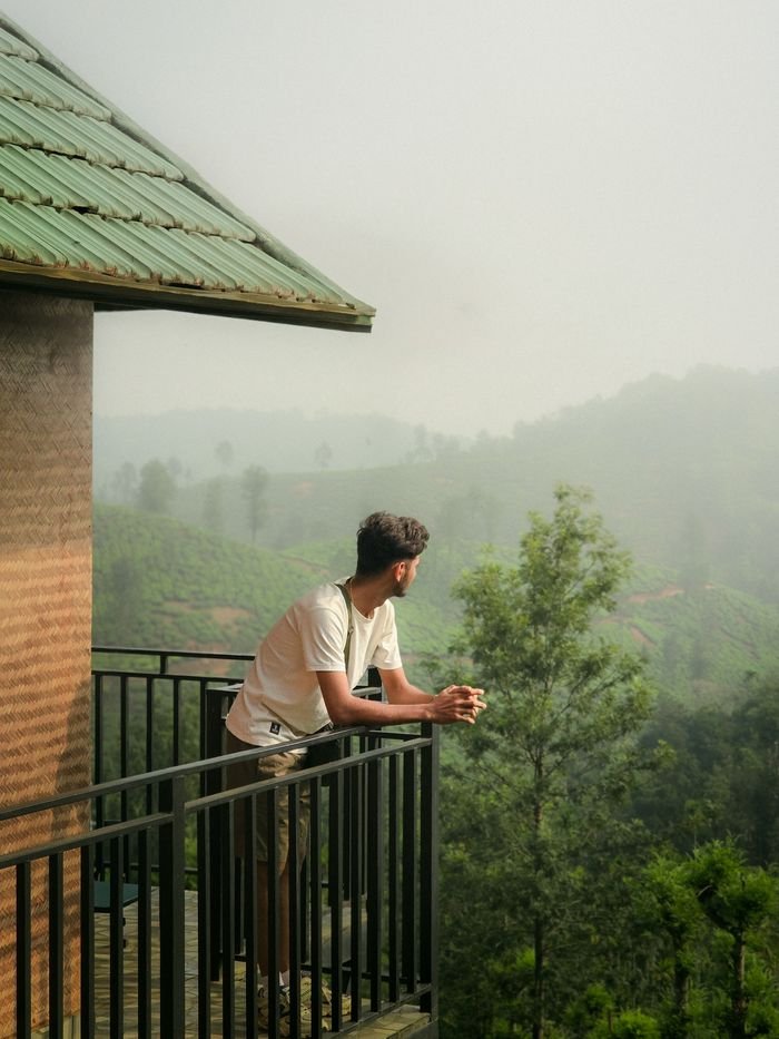 pexels photo 37975020 37975020 A man stands on a balcony gazing at fog-covered lush green hills, creating a serene and contemplative scene.
